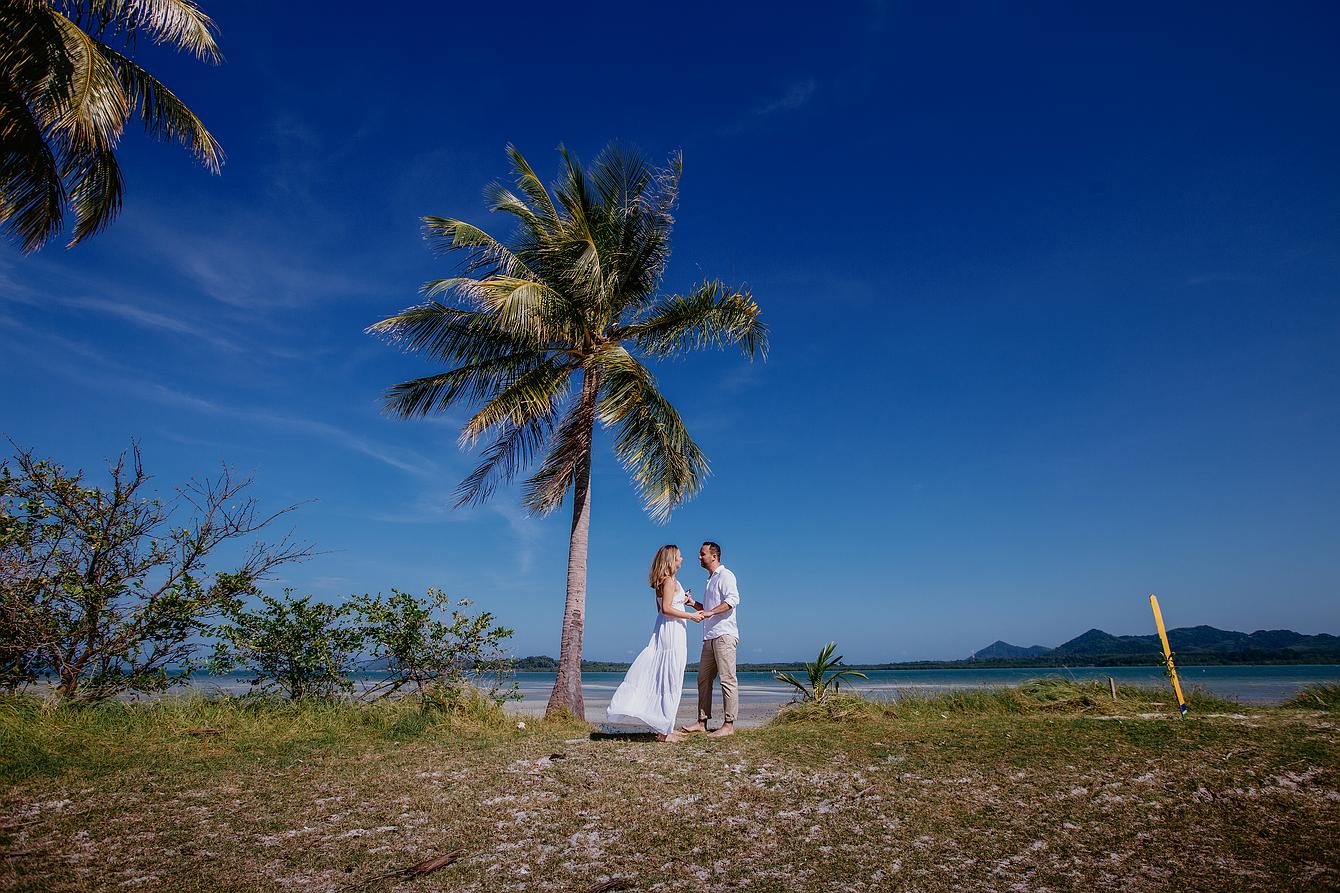 Hochzeit zu zweit. Abbildung Brautpaar steht unter eine Palme am weißen Sandstrand mit tief blauen Himmel