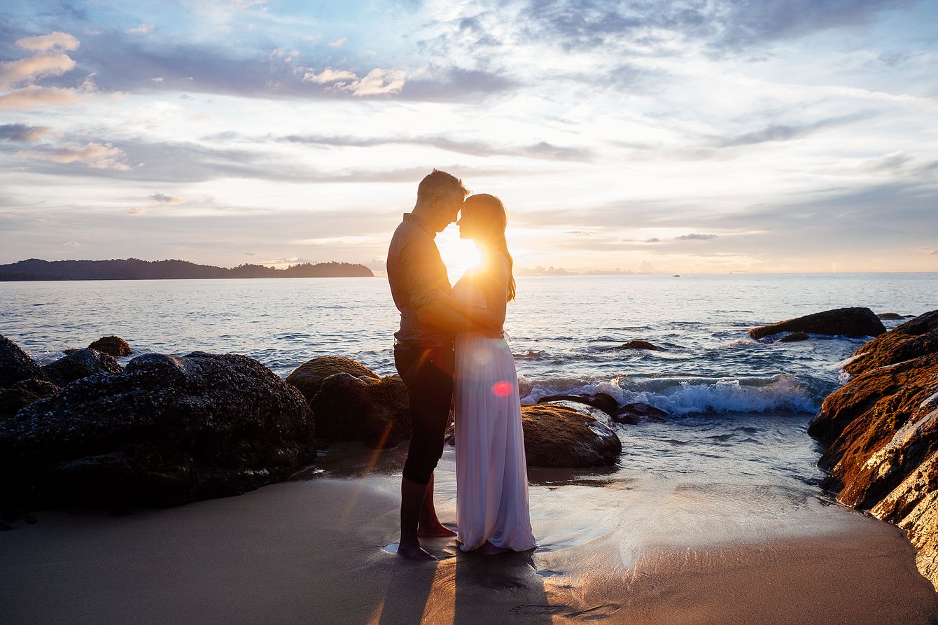 Heiraten am Strand. Abbildung: Brautpaar steht eng Umschlungen am Meer und genießt den Sonnenuntergang