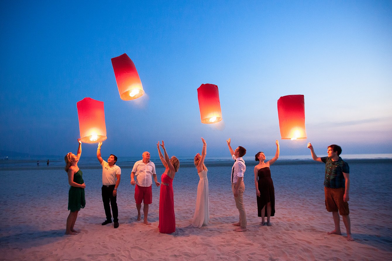 Eine Gruppe von Hochzeitsgästen lässtHimmelslaternen am Strand in Thailand steigen